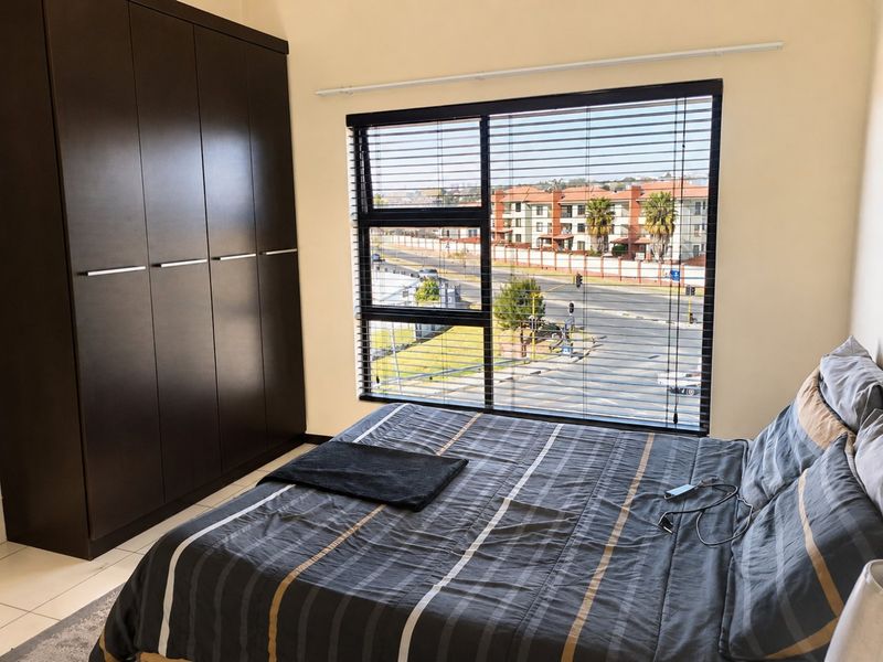 A well-maintained bedroom featuring dark built-in wardrobes, tiled flooring, and large windows with venetian blinds offering an urban street view.