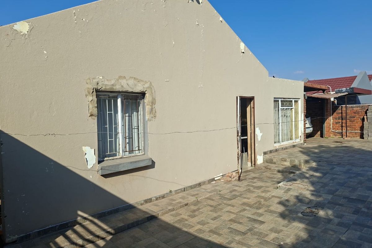 Rear exterior view of the property featuring a tiled patio area, security bars on windows, and visible wear to the exterior wall finishes.