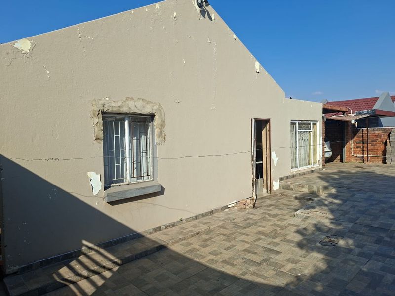 Rear exterior view of the property featuring a tiled patio area, security bars on windows, and visible wear to the exterior wall finishes.