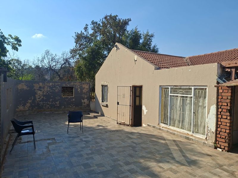 Rear exterior view of the property featuring a tiled patio area, security gate, and sliding door access, showing signs of significant exterior wear.