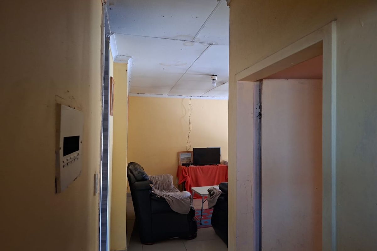 A view from a hallway into a living area featuring tiled floors and ceiling panels, showing signs of wear and water damage.