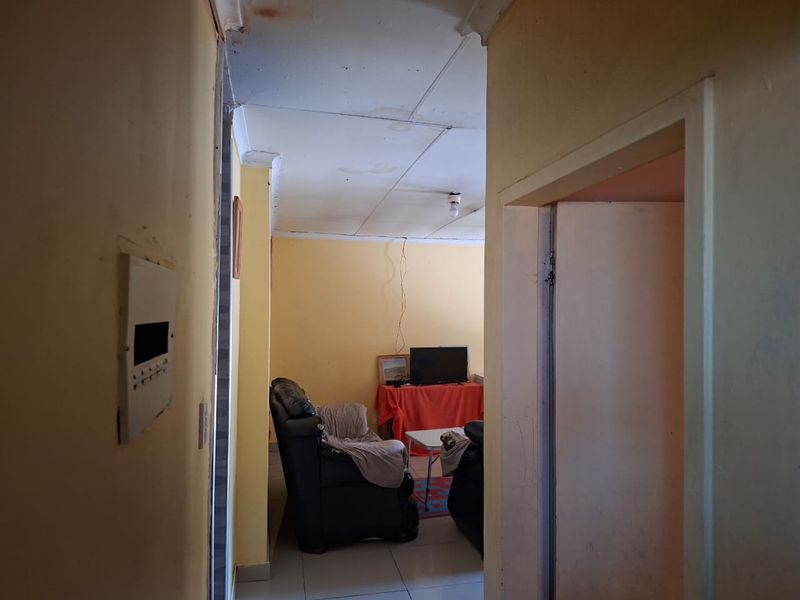 A view from a hallway into a living area featuring tiled floors and ceiling panels, showing signs of wear and water damage.