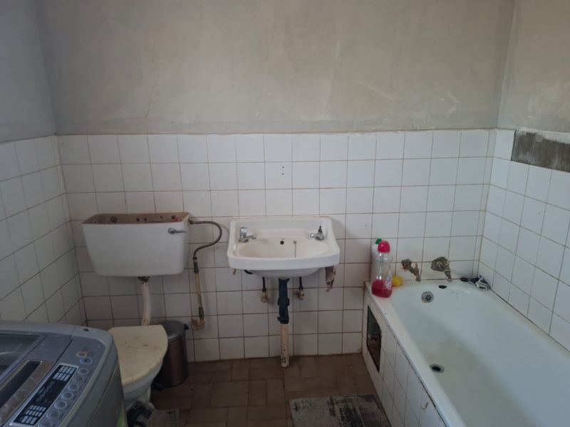 A bathroom in need of renovation, featuring a wall-mounted basin, bathtub, and toilet cistern with unfinished wall surfaces and dated tiling.