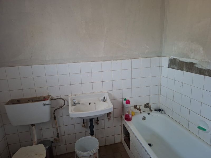 A bathroom in need of renovation, featuring a wall-mounted basin, bathtub, and toilet cistern with unfinished wall surfaces and exposed plumbing.