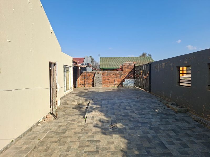 A paved rear courtyard area featuring a brick boundary wall, metal security gate, and access to the main dwelling via a sliding door.