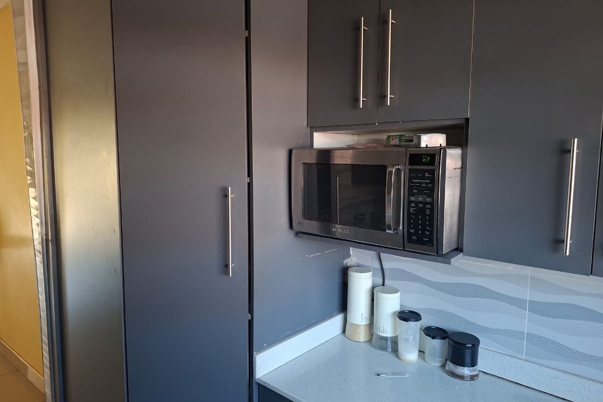 A modern kitchen area featuring dark grey cabinetry, a built-in microwave, stone countertops, and a decorative tiled backsplash.