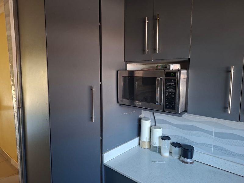 A modern kitchen area featuring dark grey cabinetry, a built-in microwave, stone countertops, and a decorative tiled backsplash.