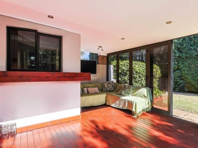 Covered outdoor patio featuring timber decking, stone pillar accents, and large sliding glass doors providing seamless access to the garden.