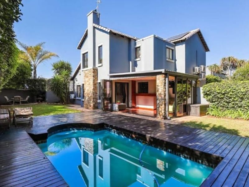 Rear view of a two-story house featuring a swimming pool with timber decking, a covered patio area, and stone-clad architectural details.
