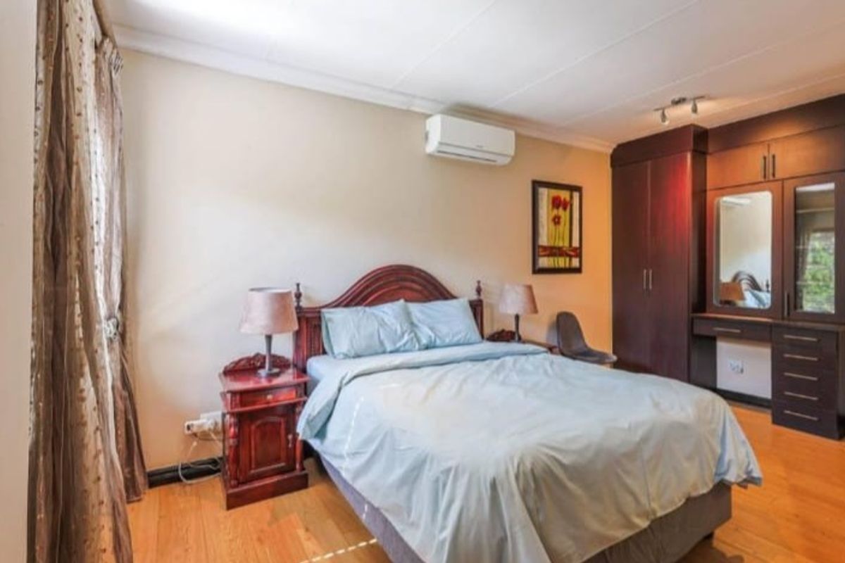A well-maintained bedroom featuring built-in dark wood cabinetry, a vanity area, laminate flooring, and a wall-mounted air conditioning unit.