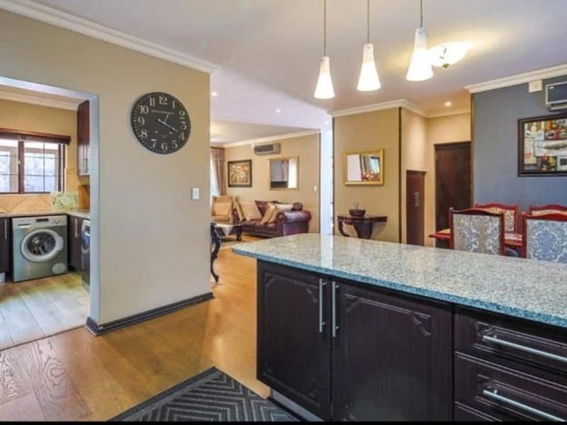 Open-plan living and kitchen area featuring a granite-topped island, dark wood cabinetry, integrated laundry space, and modern recessed lighting throughout.