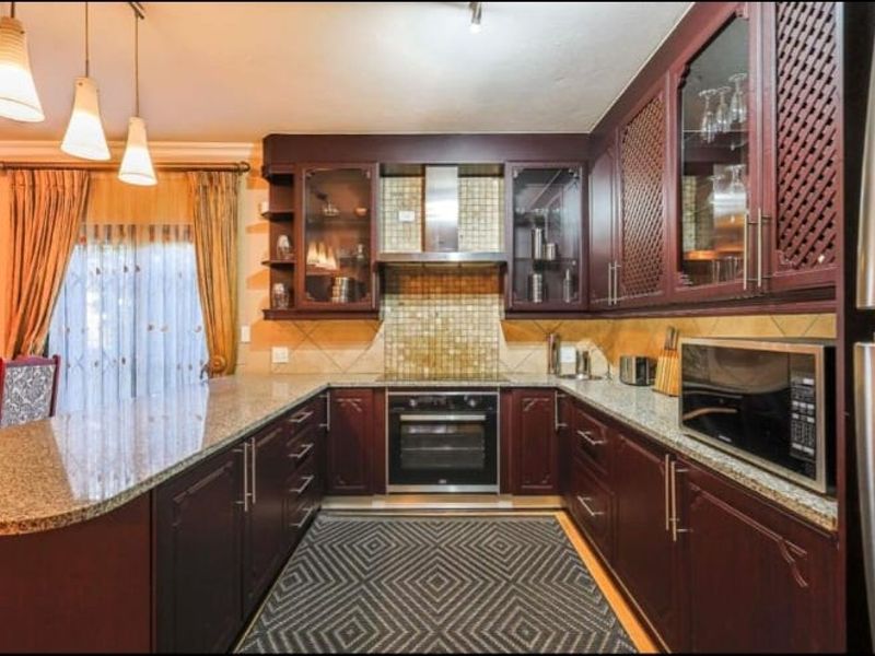 A well-appointed kitchen featuring dark wood cabinetry, granite countertops, a mosaic tile backsplash, and integrated stainless steel appliances.