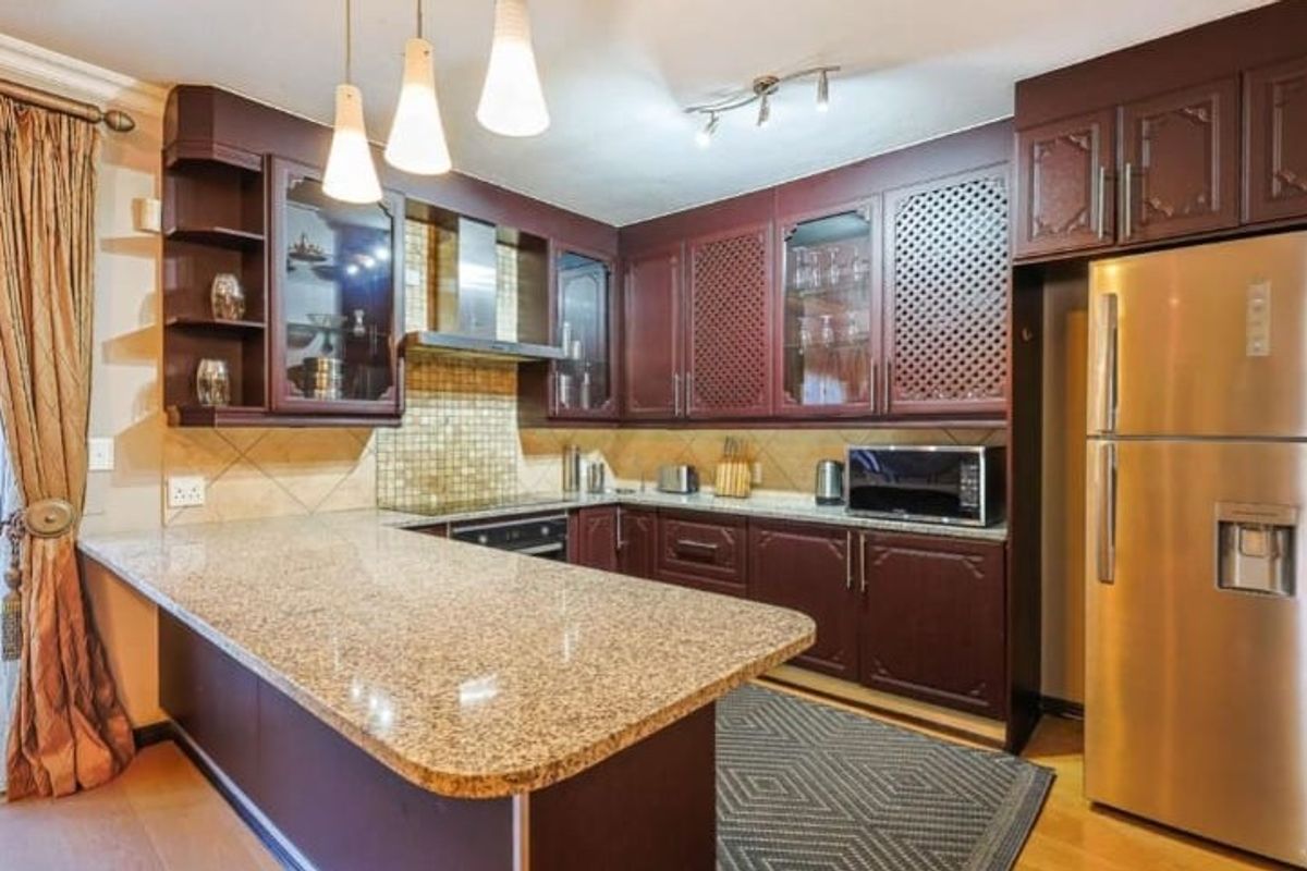 A functional kitchen featuring dark wood cabinetry, granite countertops, a mosaic tile backsplash, and integrated appliances with a breakfast bar area.