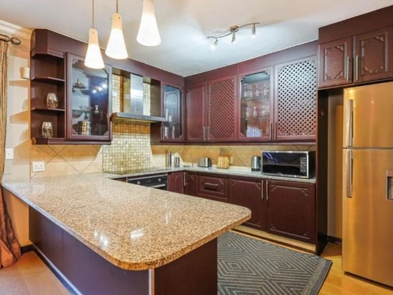 A functional kitchen featuring dark wood cabinetry, granite countertops, a mosaic tile backsplash, and integrated appliances with a breakfast bar area.