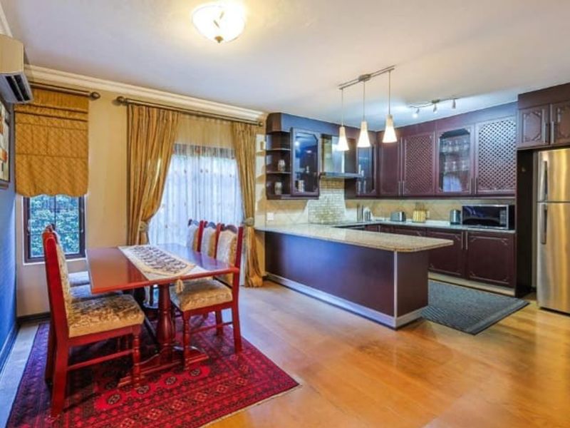 Open-plan kitchen and dining area featuring dark wood cabinetry, granite countertops, hardwood flooring, and integrated lighting.