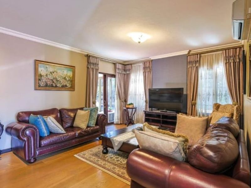 A well-maintained living room featuring hardwood flooring, crown molding, and a wall-mounted air conditioning unit, with direct access to the outdoor area.