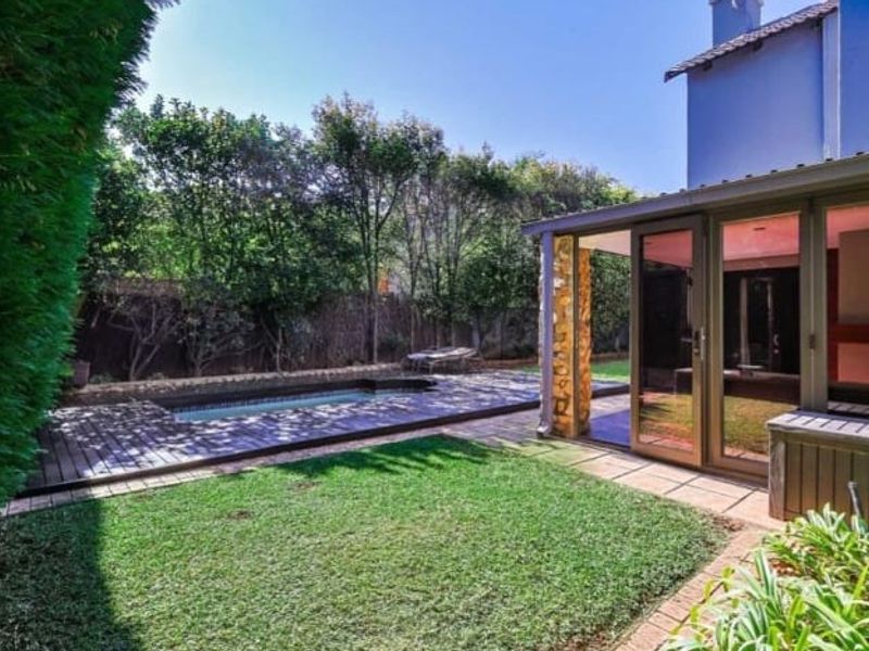 A private backyard featuring a swimming pool with wooden decking, a manicured lawn, and a covered patio area with sliding glass doors.