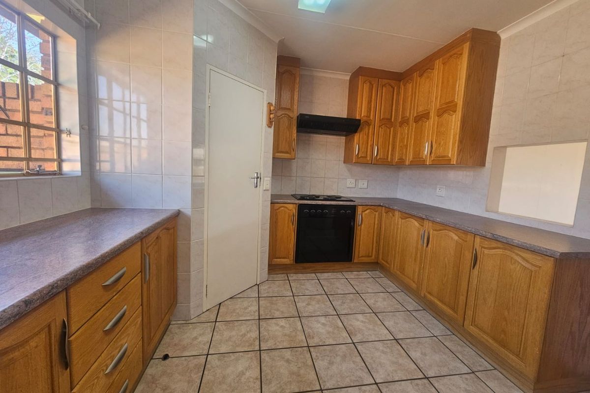 A functional kitchen featuring wooden cabinetry, laminate countertops, built-in oven, hob, extractor fan, and tiled flooring.