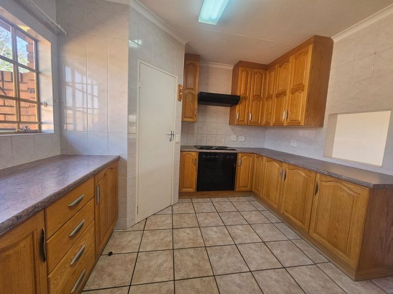 A functional kitchen featuring wooden cabinetry, laminate countertops, built-in oven, hob, extractor fan, and tiled flooring.
