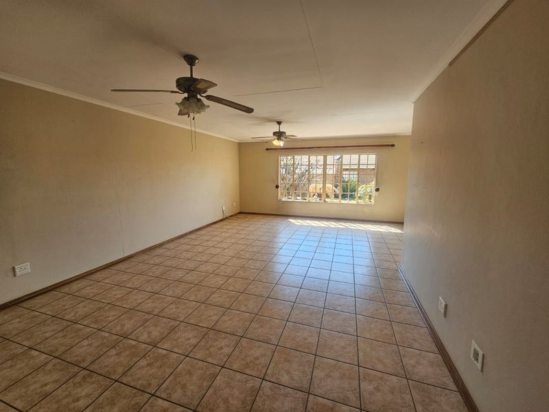 Spacious, empty living area featuring neutral tiled flooring, dual ceiling fans, and a large window providing natural light.