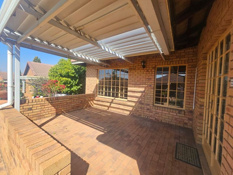 A covered outdoor patio featuring brick paving, a louvred roof system, and classic timber-framed windows and doors, offering a functional space for outdoor living.