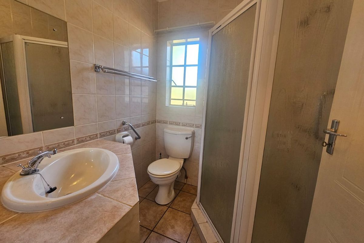 A functional bathroom featuring a vanity basin, a shower enclosure, and a toilet, finished with neutral wall and floor tiling.