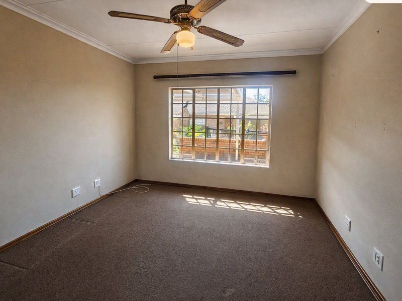 A vacant bedroom featuring neutral walls, carpeted flooring, a ceiling fan, and a window fitted with security bars.