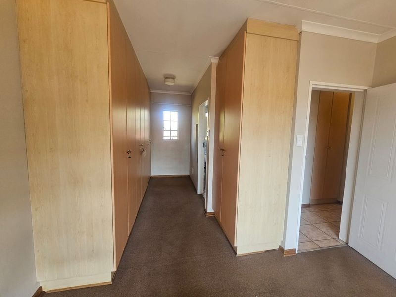 A functional hallway featuring extensive built-in cabinetry for storage, neutral wall finishes, and carpeted flooring.
