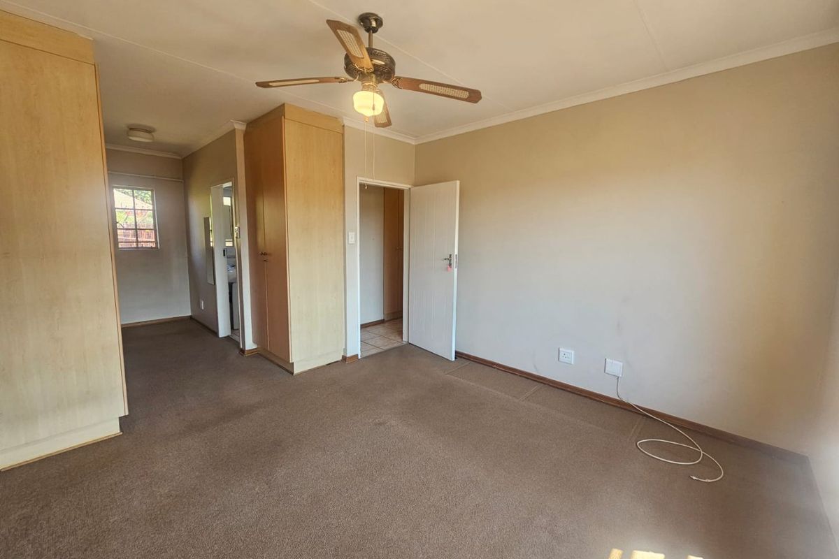 Spacious bedroom featuring built-in cupboards, a ceiling fan, and neutral carpeting, offering a blank canvas for personalization.