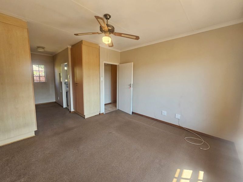 Spacious bedroom featuring built-in cupboards, a ceiling fan, and neutral carpeting, offering a blank canvas for personalization.