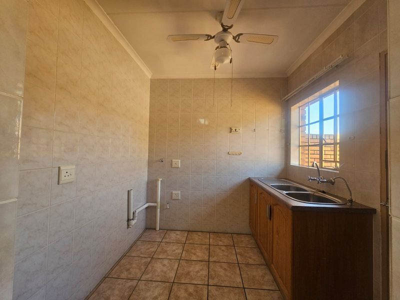A functional laundry room featuring tiled walls and flooring, a double sink with built-in cabinetry, and plumbing connections for appliances.