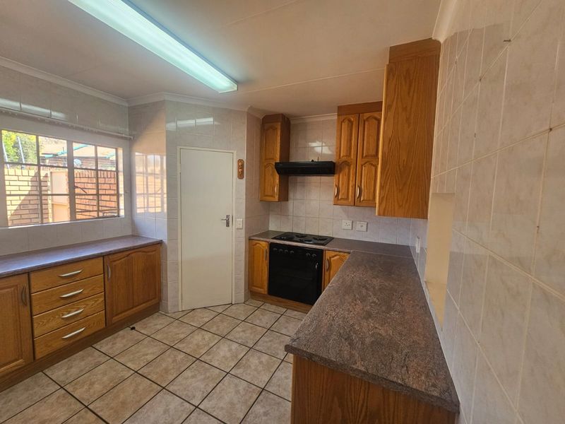 A functional kitchen featuring built-in wooden cabinetry, laminate countertops, tiled flooring, and integrated cooking appliances, offering a clean and practical workspace.