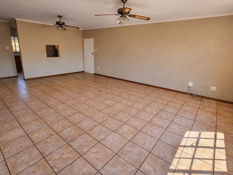 A spacious, empty living area featuring neutral wall tones, tiled flooring, and dual ceiling fans, offering a versatile blank canvas for interior design.