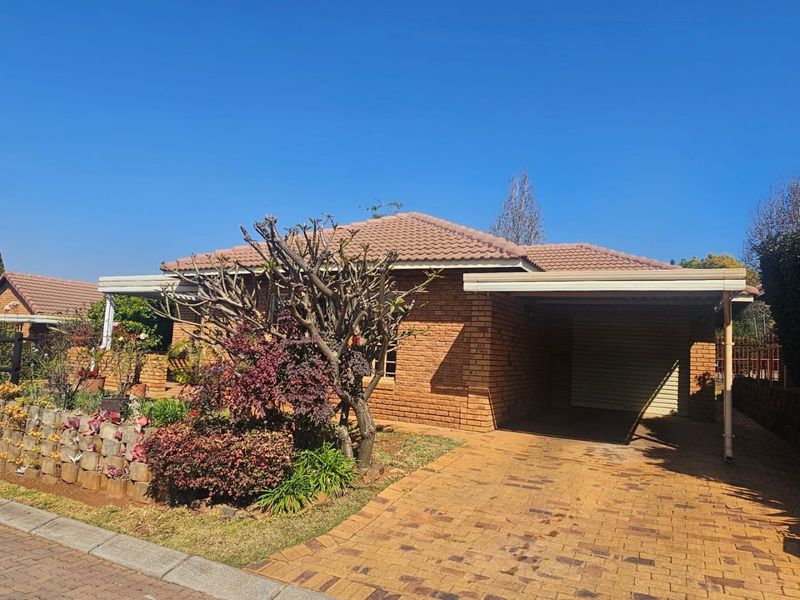 Front view of a face brick house featuring a paved driveway, integrated carport with a roller door, and a landscaped front garden with a retaining wall.
