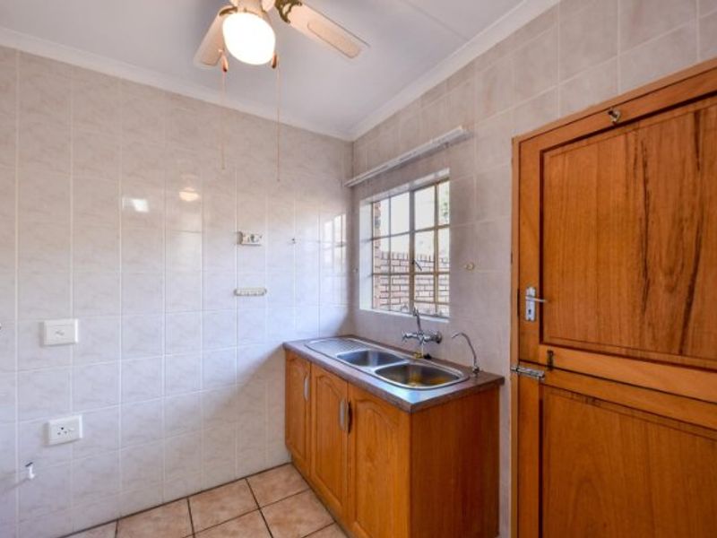 A functional laundry room featuring tiled walls, tiled flooring, a double sink with wooden cabinetry, and a ceiling fan.