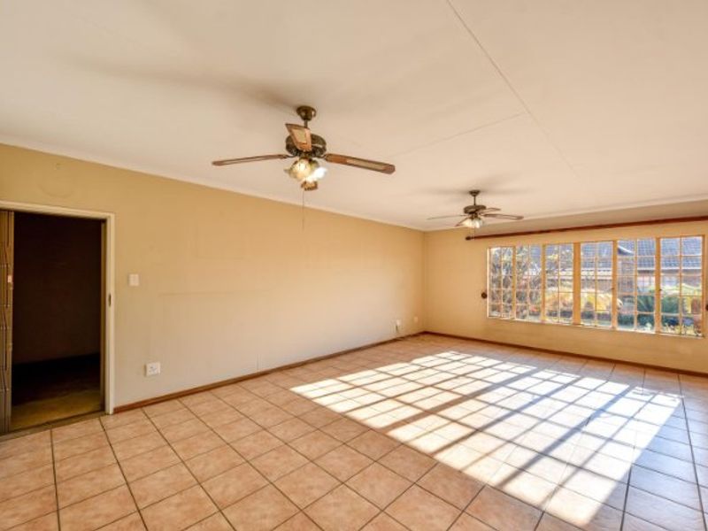 Spacious, empty living area featuring tiled flooring, dual ceiling fans, and large windows that provide ample natural light.