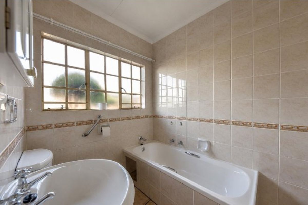 A functional bathroom featuring a built-in bathtub, pedestal washbasin, toilet, and neutral ceramic wall tiling with a decorative border.