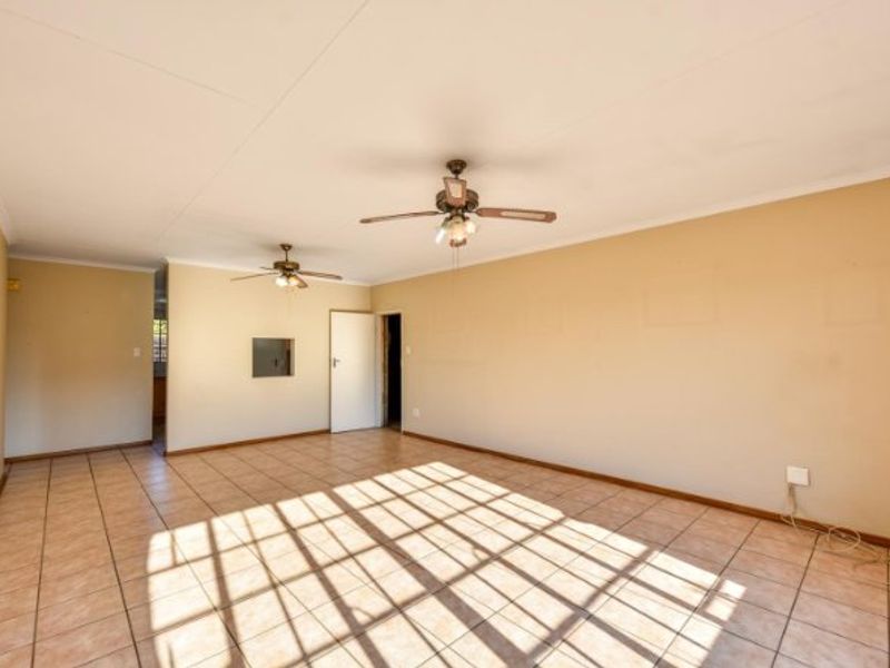 Spacious, empty living area featuring neutral tiled flooring and dual ceiling fans, offering a blank canvas for interior design.