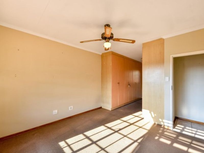 An empty bedroom featuring built-in wooden cupboards, a ceiling fan, and carpeted flooring, offering a blank canvas for personalization.