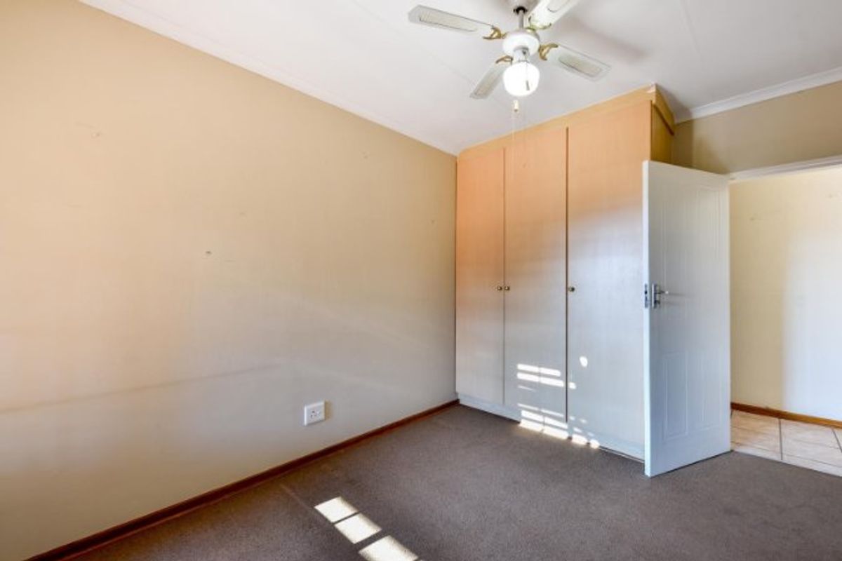 A vacant bedroom featuring built-in wooden cupboards, a ceiling fan, and carpeted flooring, offering a blank canvas for personalization.