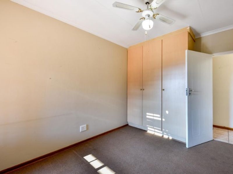 A vacant bedroom featuring built-in wooden cupboards, a ceiling fan, and carpeted flooring, offering a blank canvas for personalization.