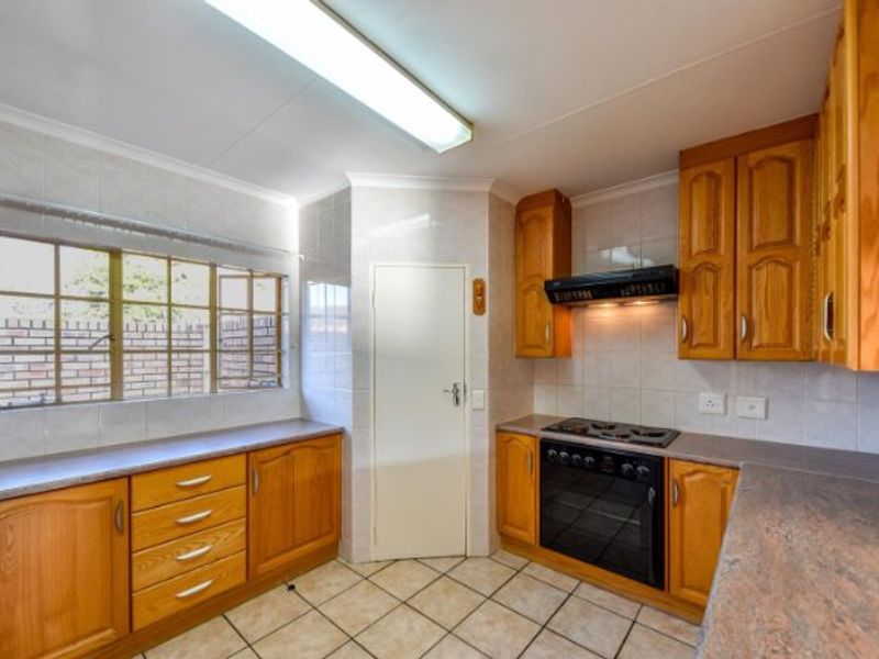 A functional kitchen featuring traditional wooden cabinetry, laminate countertops, built-in oven, electric hob, and tiled flooring with ample natural light.