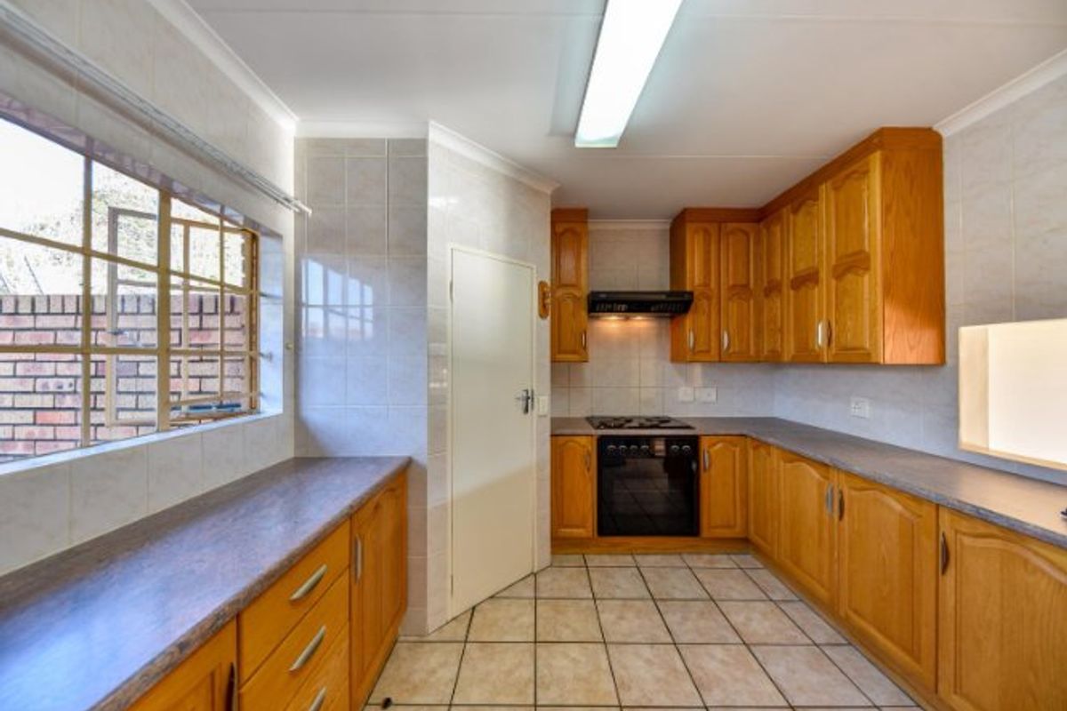 A functional kitchen featuring wooden cabinetry, laminate countertops, a built-in oven with gas hob, and tiled flooring throughout.
