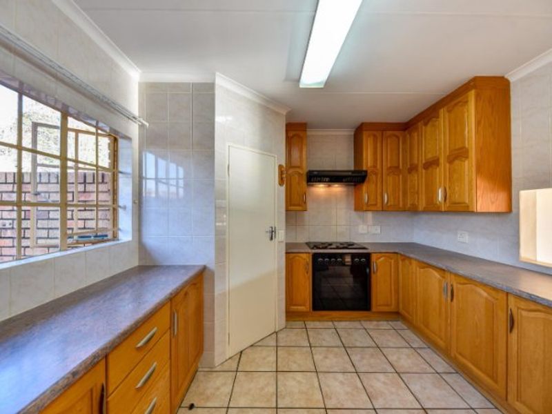 A functional kitchen featuring wooden cabinetry, laminate countertops, a built-in oven with gas hob, and tiled flooring throughout.