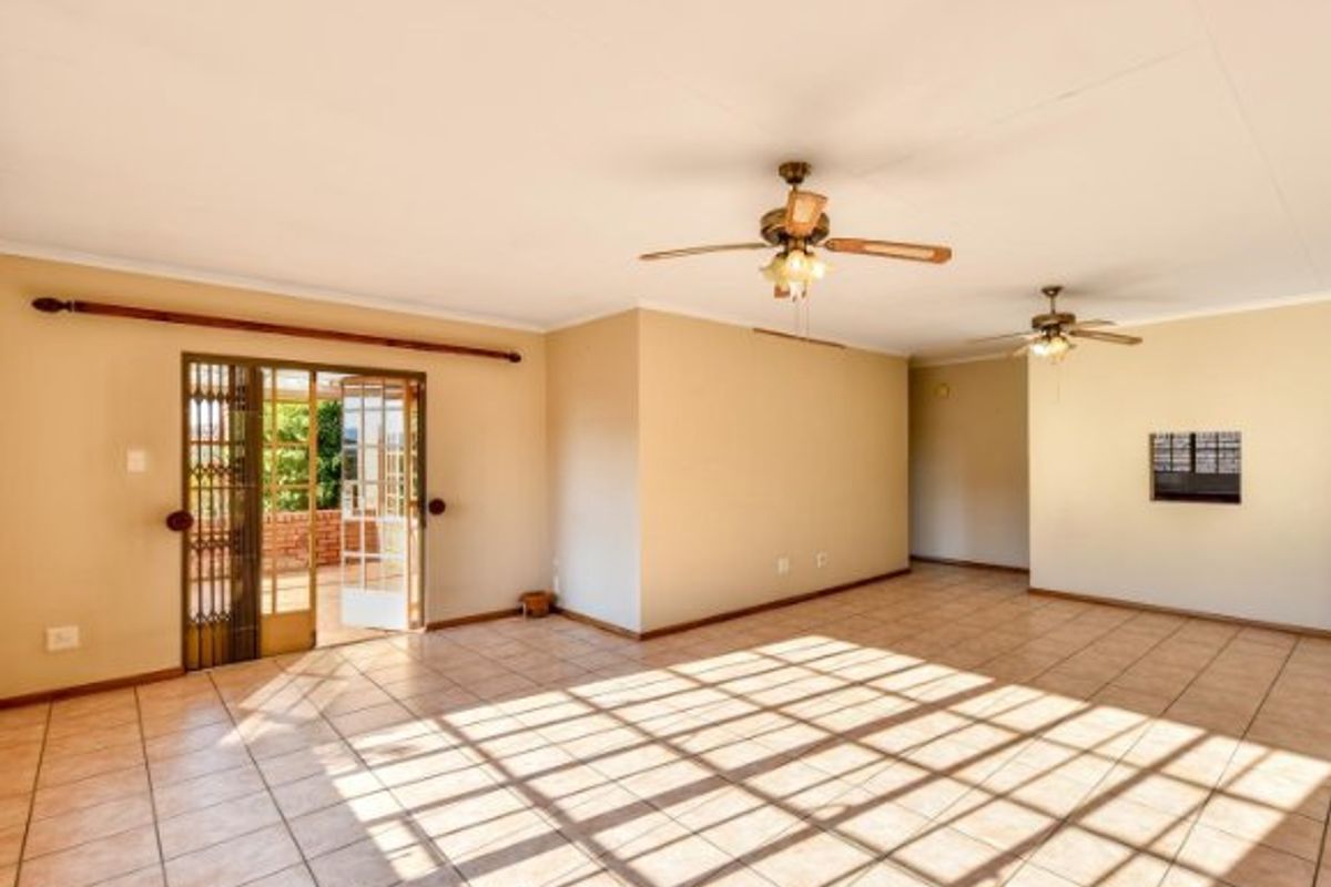 Spacious, open-plan living area featuring neutral tiled flooring, dual ceiling fans, and direct access to an outdoor patio through a sliding glass door.