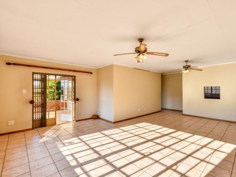 Spacious, open-plan living area featuring neutral tiled flooring, dual ceiling fans, and direct access to an outdoor patio through a sliding glass door.