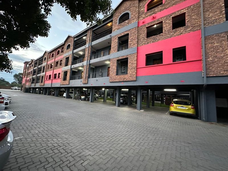 Exterior view of a multi-story apartment complex featuring brick and painted facade, with ground-level covered parking and paved driveway access.