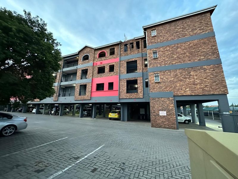 Exterior view of a multi-story apartment building featuring a face brick facade, covered ground-level parking, and private balconies.