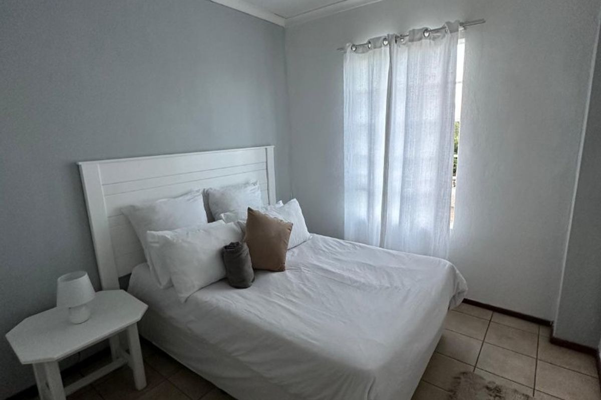 A functional bedroom featuring tiled flooring, neutral wall tones, and a ceiling-mounted spotlight fixture, providing a clean and simple living space.