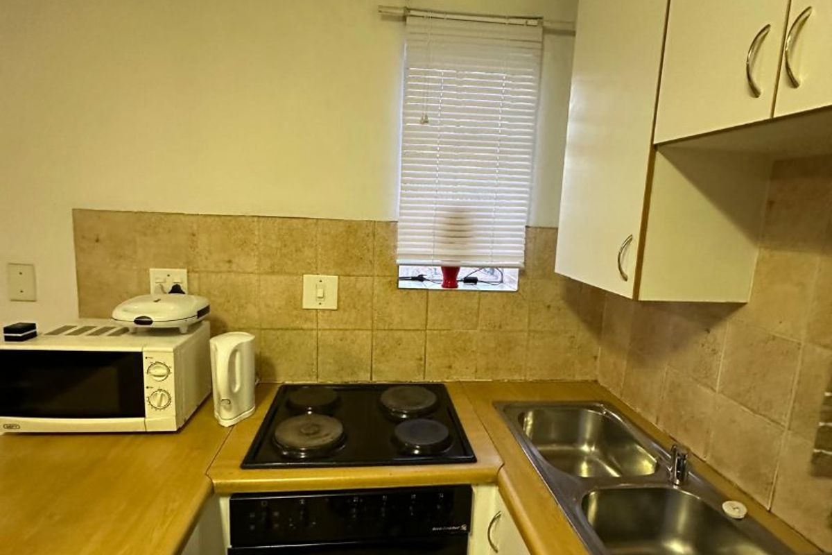 Compact kitchen featuring built-in cabinetry, laminate countertops, an electric hob and oven, and a double stainless steel sink with tiled backsplash.